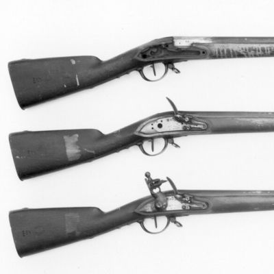 A black and white image of three muskets, each bound by three bands around the barrel, with carved cheek rest in the buttstock. 