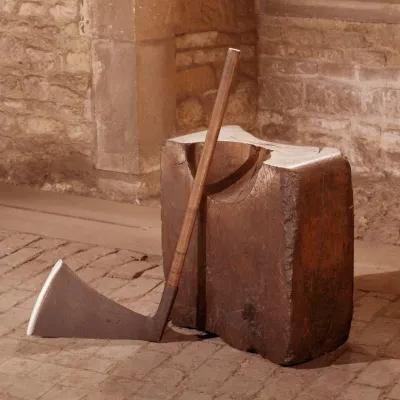 A colour photograph of an axe leaning up against an executioner's block of wood
