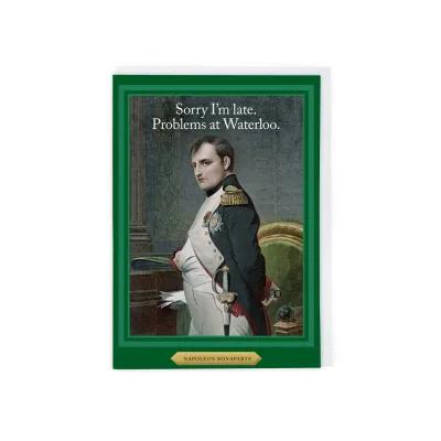 Illustrated card showing Napoleon Bonaparte in a formal setting, wearing a decorated uniform with epaulettes and medals, positioned beside a green upholstered chair. Text at the top reads: “Sorry I’m late. Problems at Waterloo,” framed by a green border.