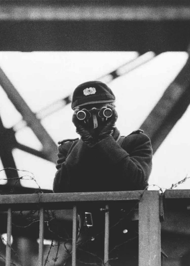 East German policeman observing through binoculars