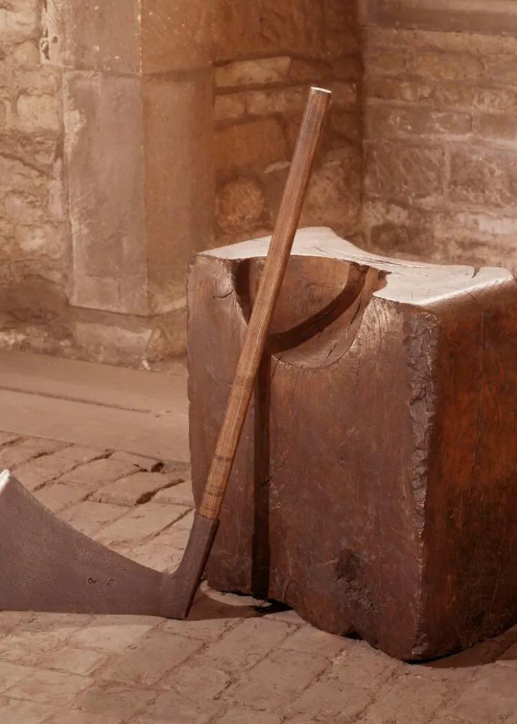 A colour photograph of an axe leaning up against an executioner's block of wood