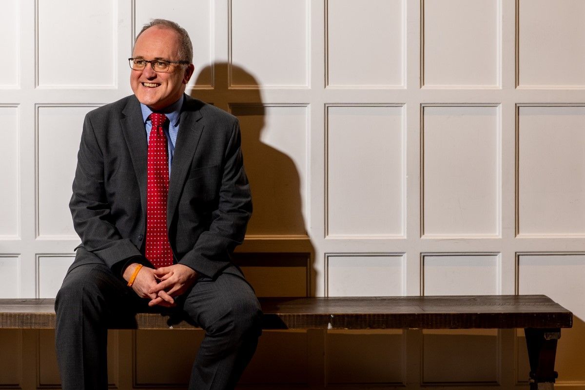 Finance Director Malcom Duncan sits in front of a white panelled wall in the War gallery