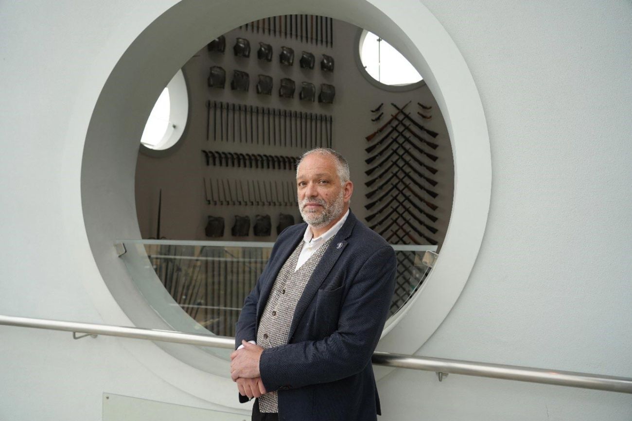 Director General Nat Edwards stands in front of a circular window in the Hall of Steel at the Royal Armouries Museum