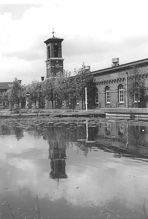 black and white image of factory building with a clocktower overlooking a lake