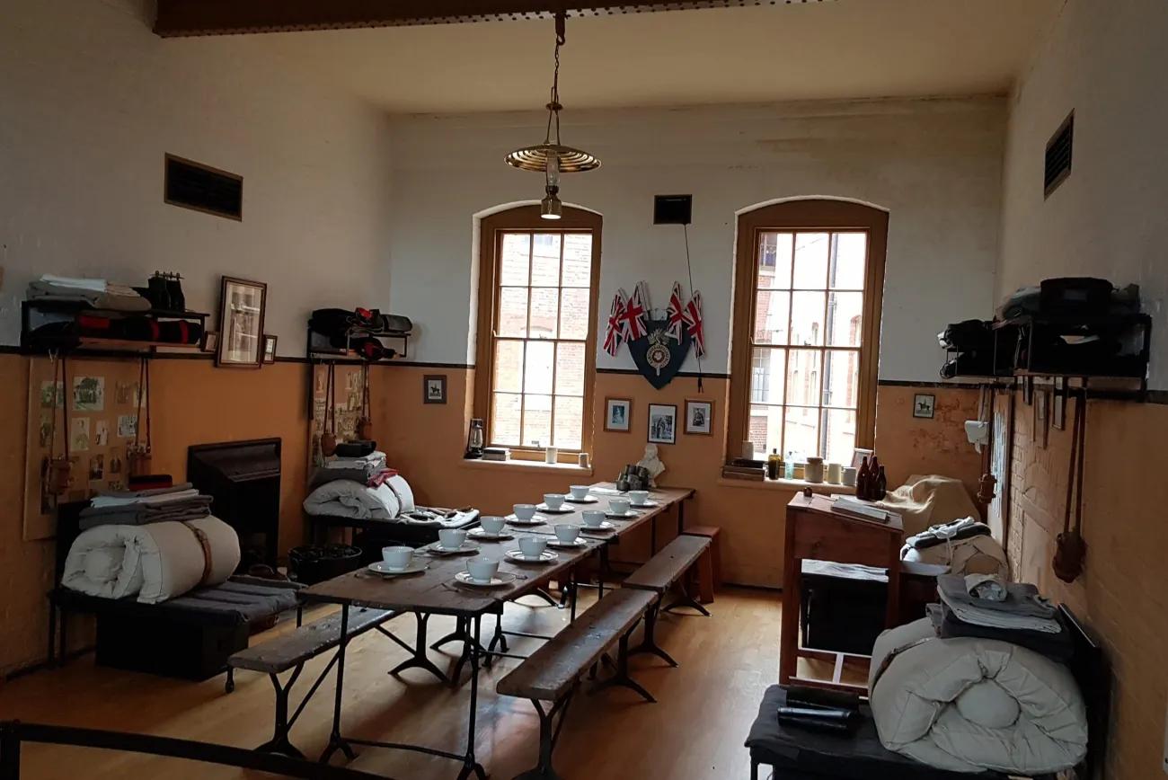 Victorian barrack room, long dining table with bench seating, resting area with soldiers belongings