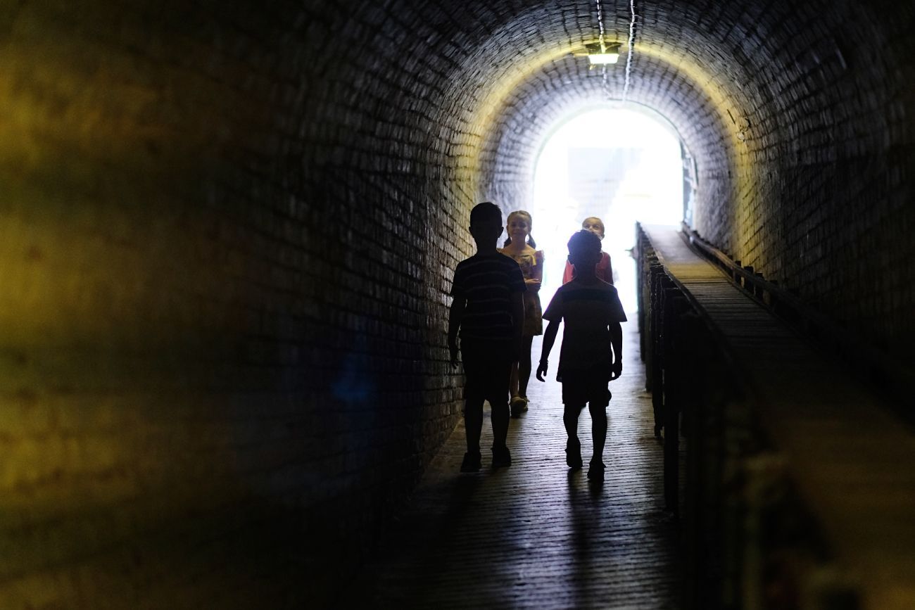 Four children in a dark tunnel with daylight shining through an arched entrance behind them