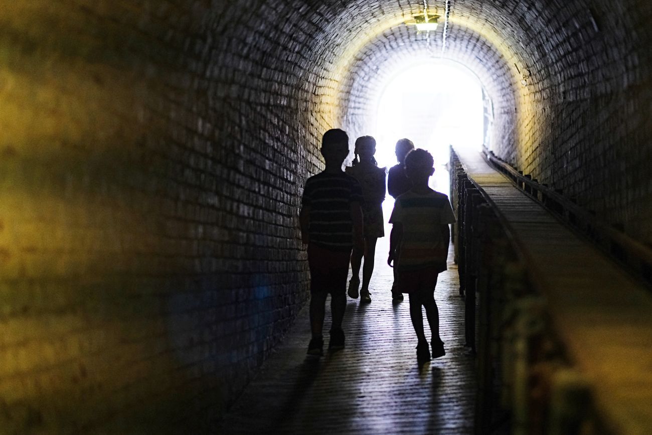 group of children in a dark tunnel with a light shining in through an arched entrance