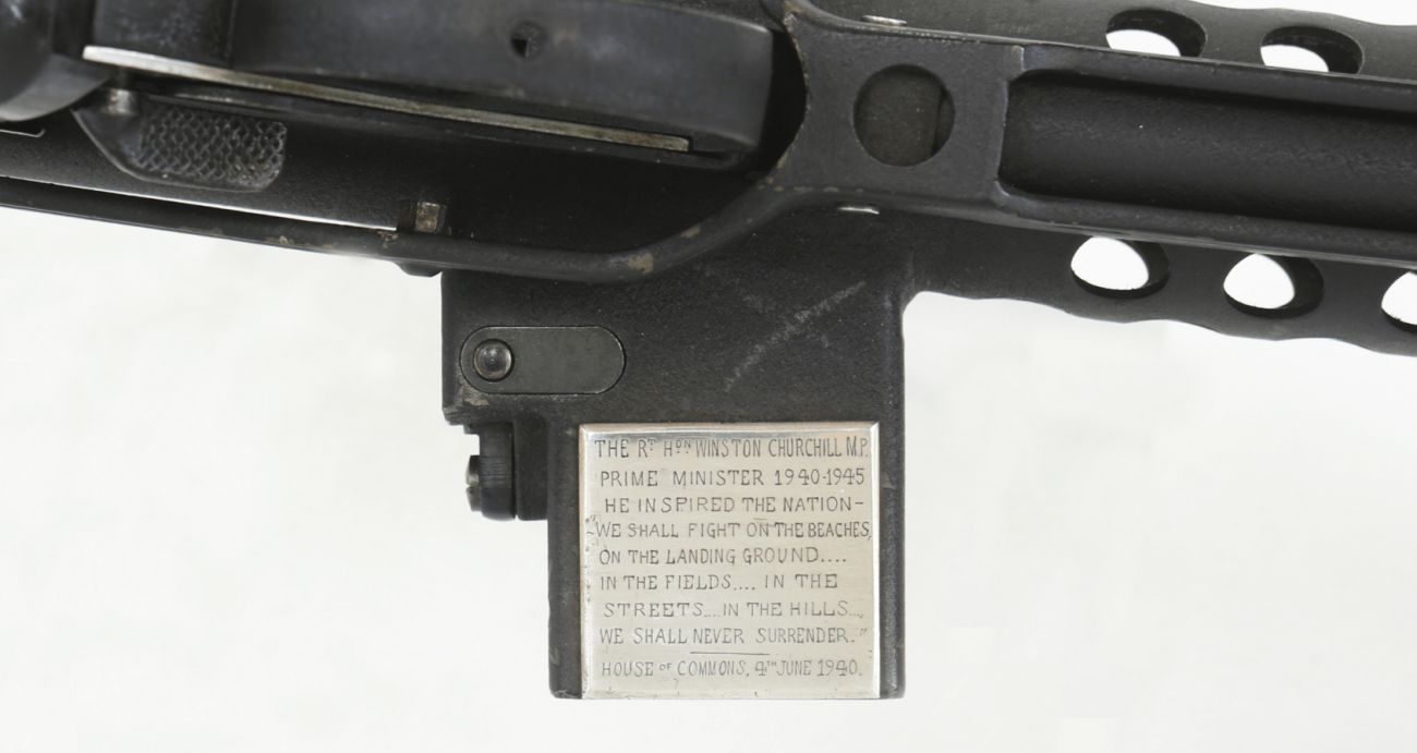 A close up of a black sub machine gun with holes and an inscription quoting Winston Churchill