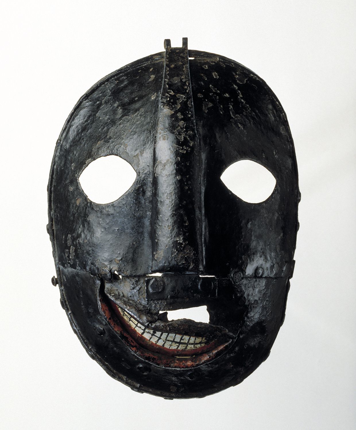 a black painted iron mask with cutout eyeholes. The mouth has painted lips and teeth creating a crooked smile