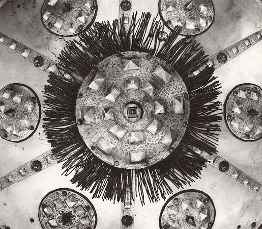 partial image of a silver coloured shield with a circular centre piece and 6 equal section radiating from the centre