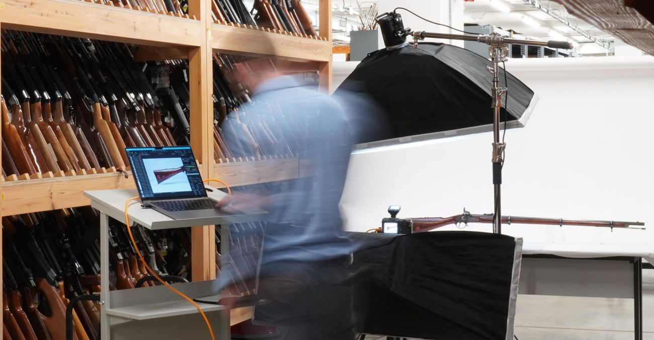 Photographer looking at image on a laptop with firearm on a table with photography lights and equipment around it.