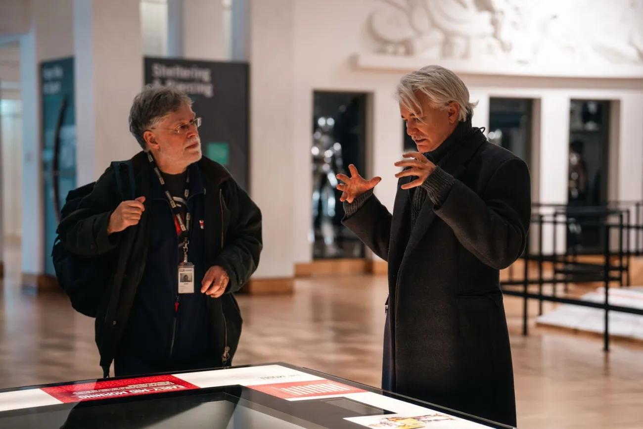 Baz Luhrmann and curator having discussion next to gallery display.