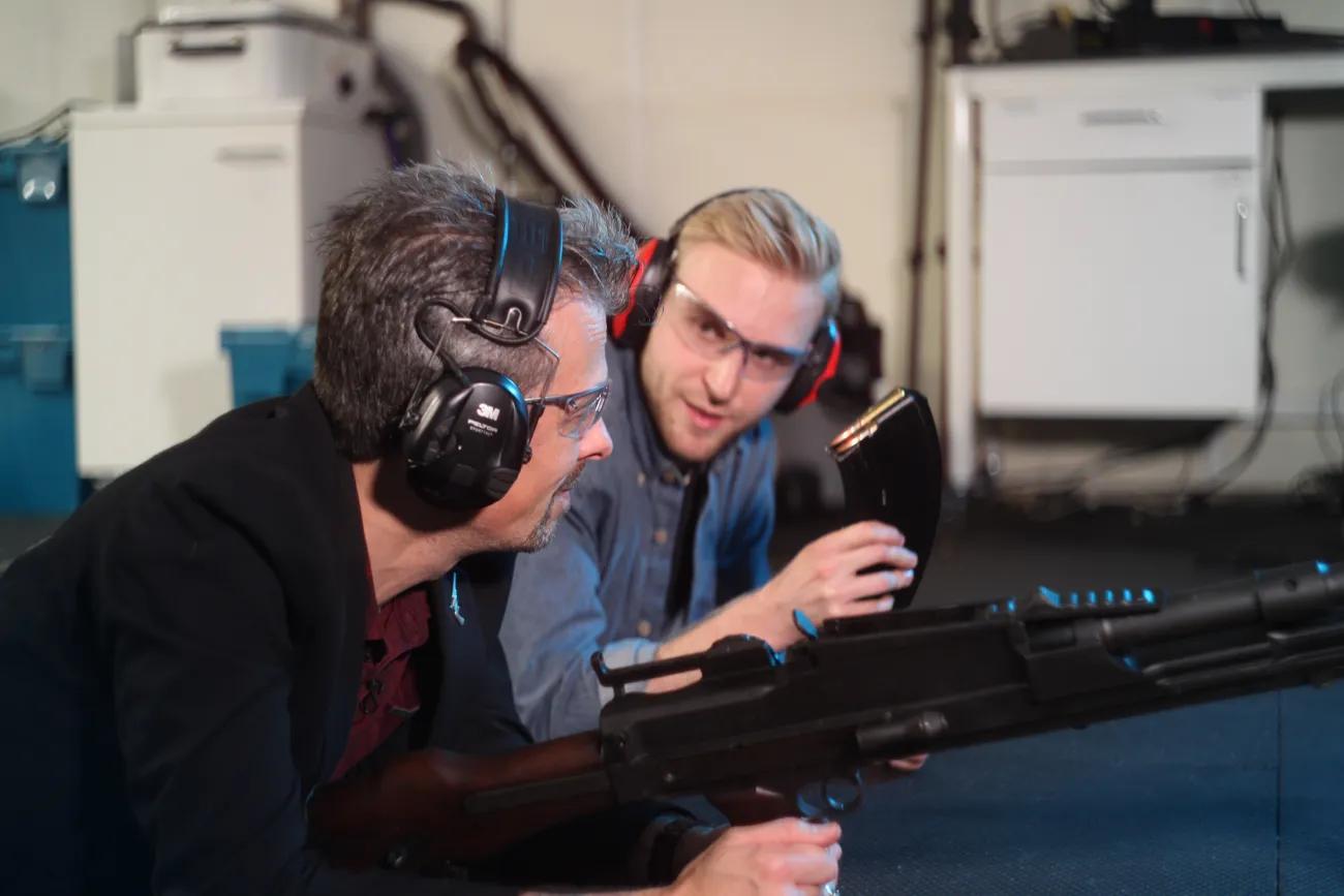 Jonathan Ferguson and Luke Tomes wearing ear defenders in discussion with Jonathan holding a bren gun