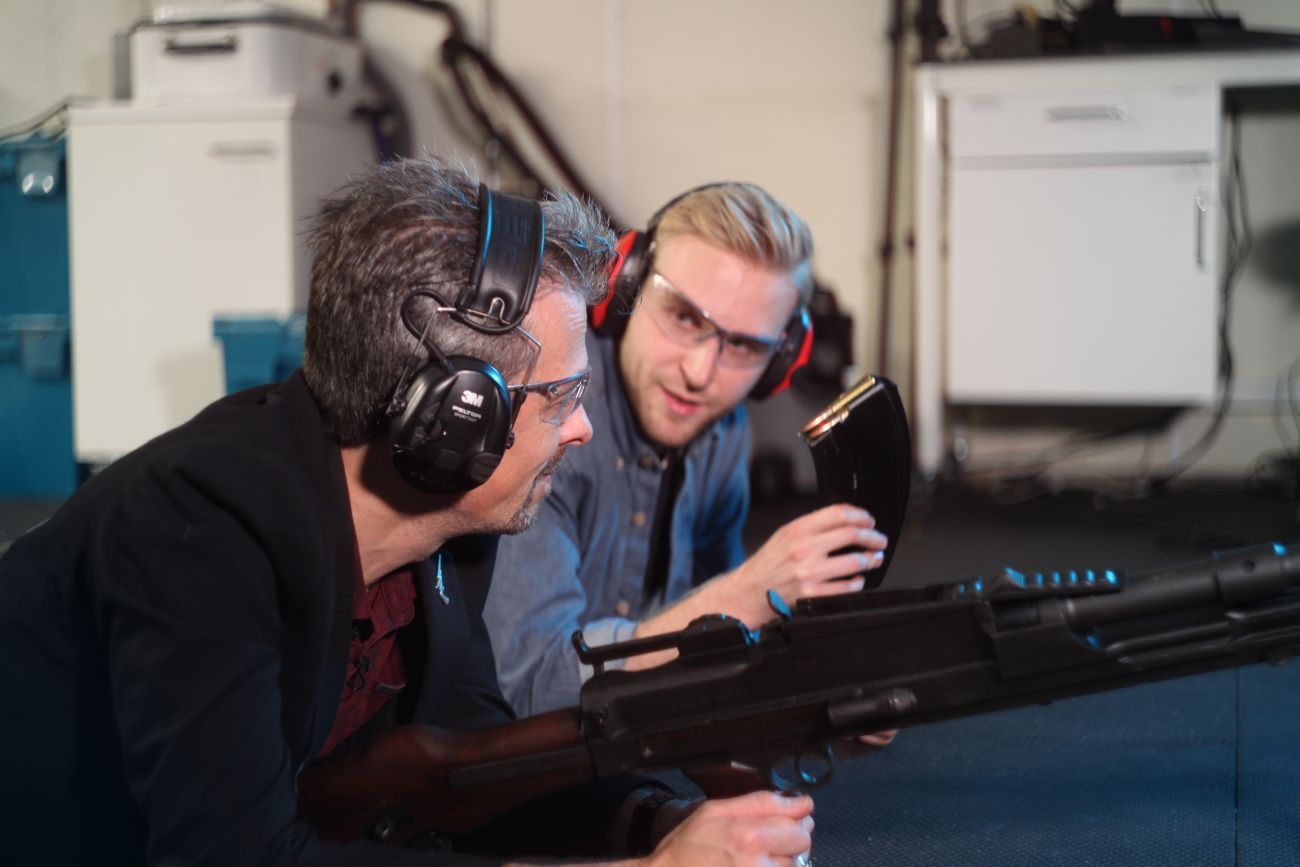 Jonathan Ferguson and Luke Tomes wearing ear defenders in discussion with Jonathan holding a bren gun