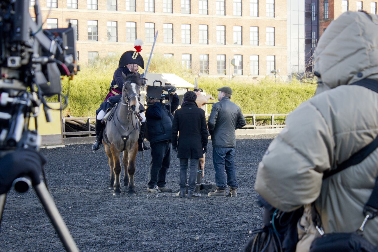 Man riding horse in Waterloo uniform and speaking to production team during filming