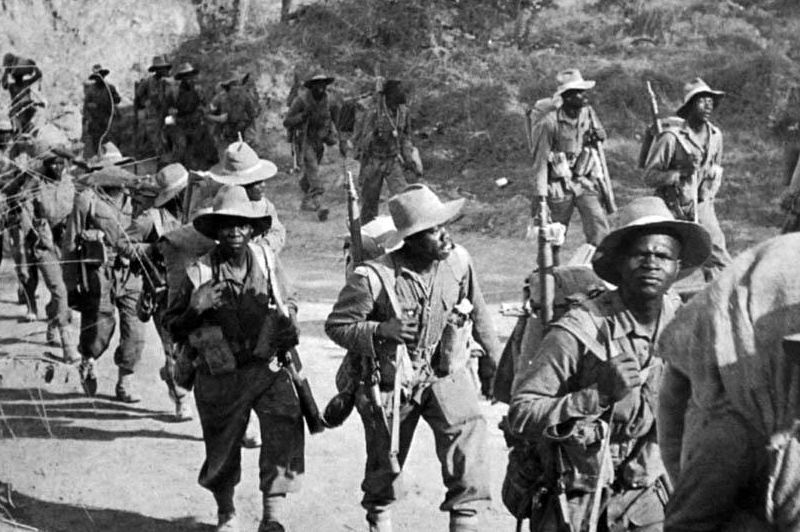 West African soldiers marching with kit and in column along a dusty road