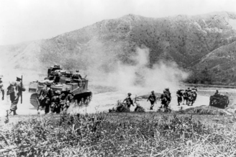 A black and white image of Gurkha soldiers advanced with tanks across a dusty road in India