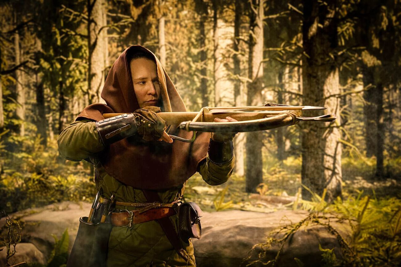 A hooded medieval hunter in the forest taking aim with their crossbow