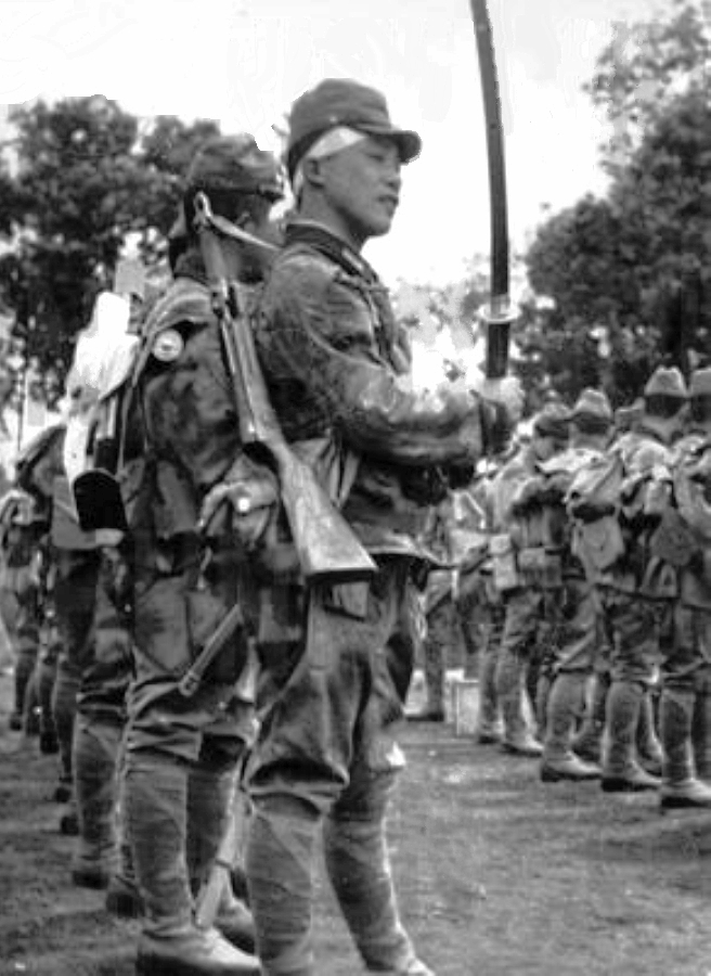 A Japanese soldier poses with a katana sword in hand and a submachine gun slung across his pack and back