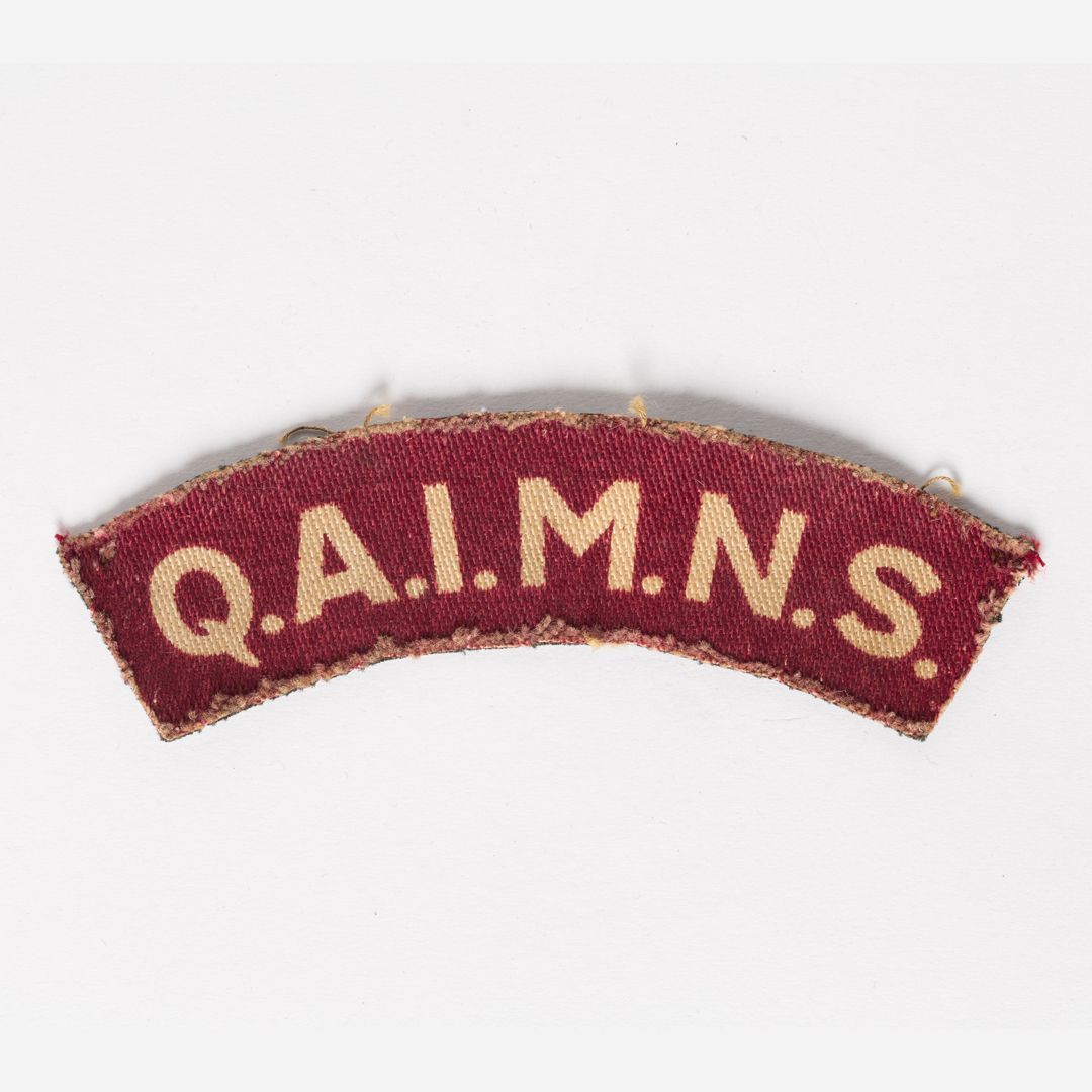 Photo of a red crescent badge with light yellow lettering spelling out Q, A, I, M, N, S.