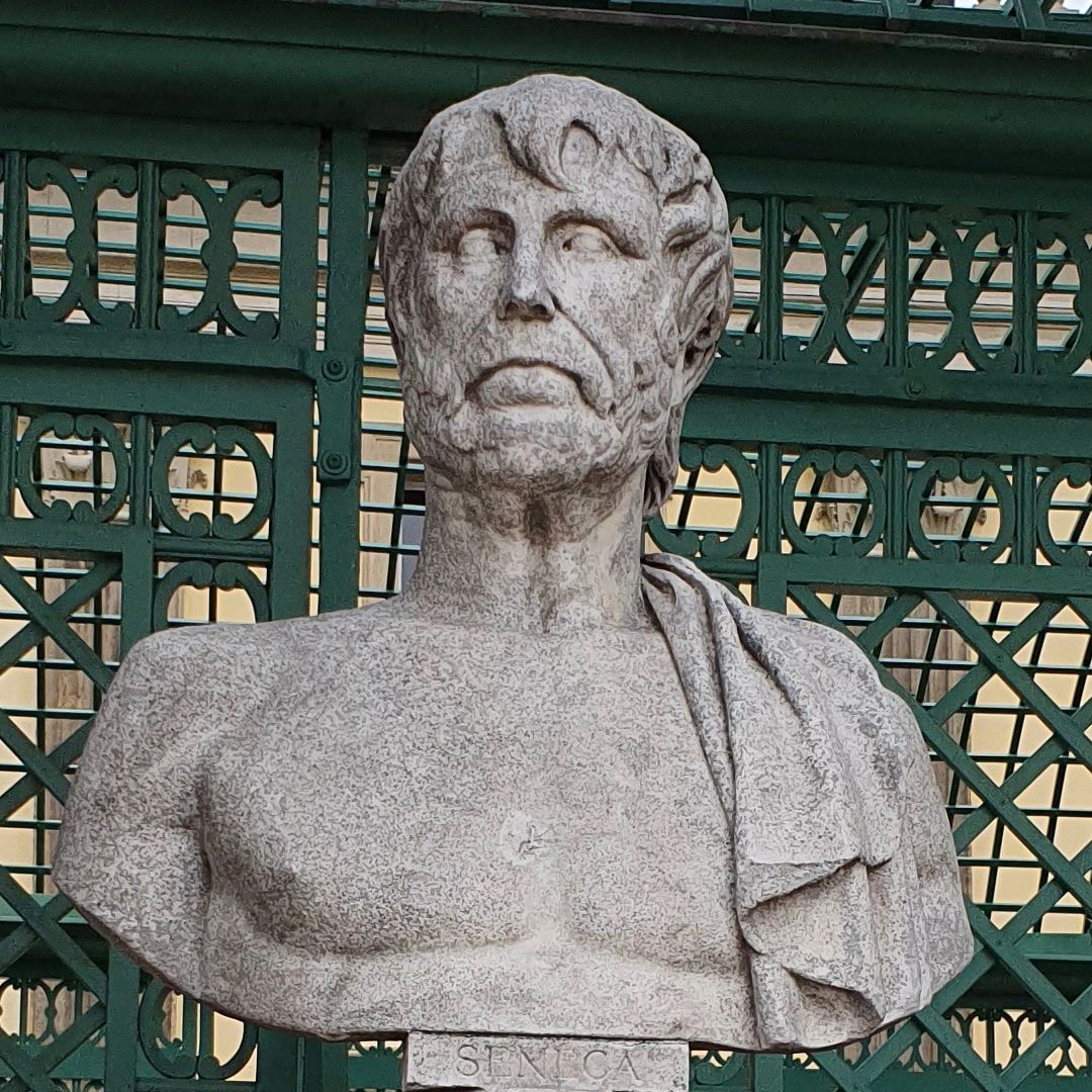 A grey stone bust of the philosopher Seneca, against green gates.