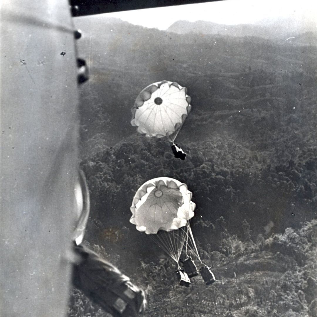 A black and white photograph of supplies being parachuted into a dense jungle