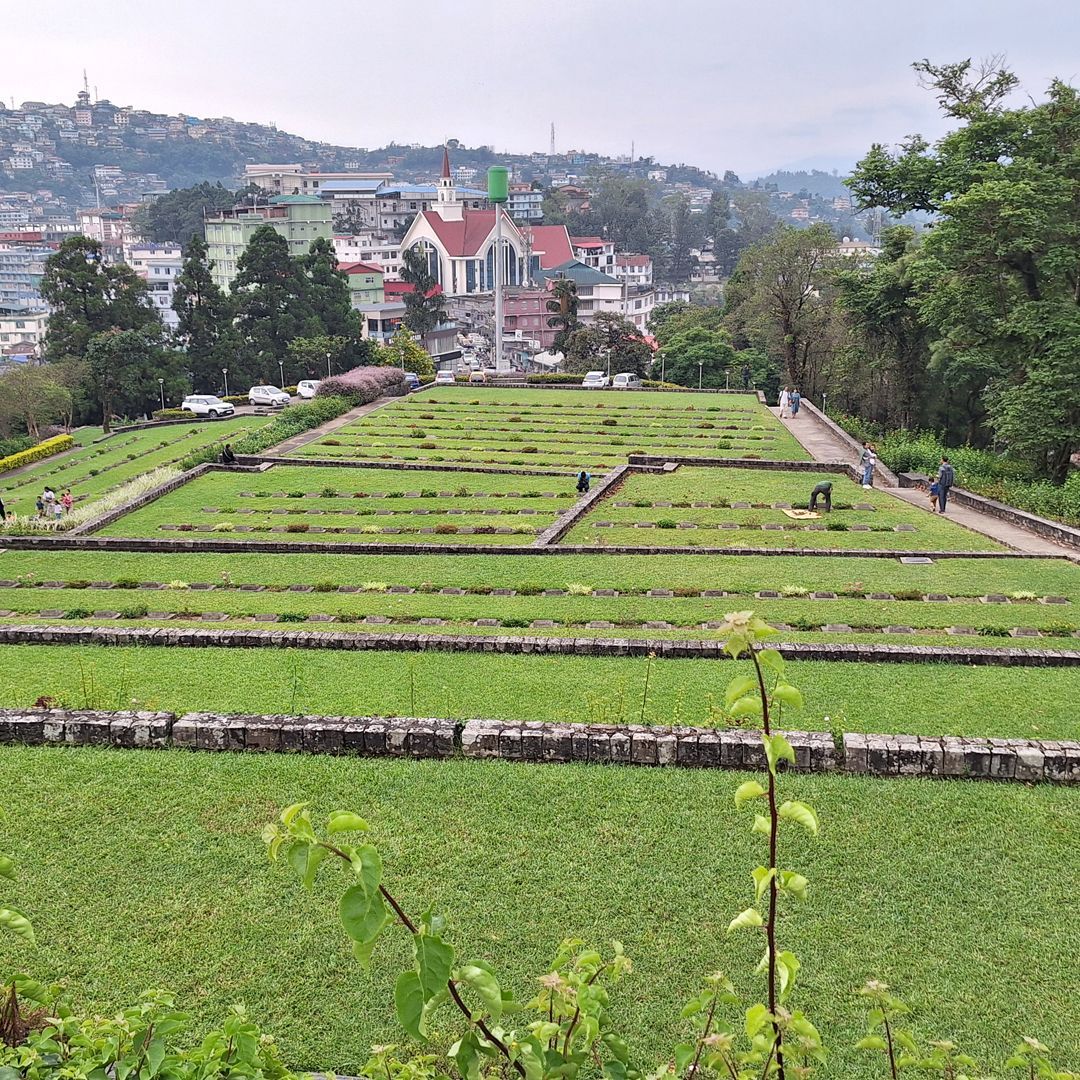 A colour image of a series of earthen tiers lined with stone leading down towards a village nestled in a hilly landscape