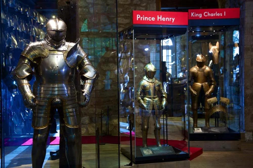 A colour photo of three suits of metal armour in descending rows. All three are held in three glass cases.