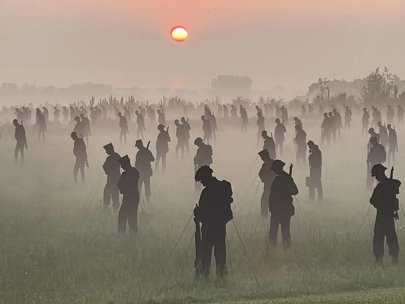 100s of life-sized silhouettes representing soldiers, in a field at dawn with mist on the ground