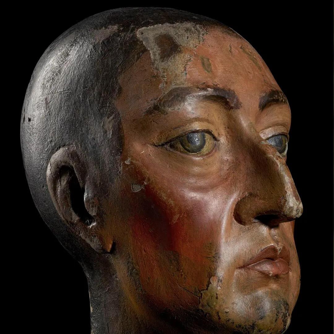 A carved wooden head against a black background