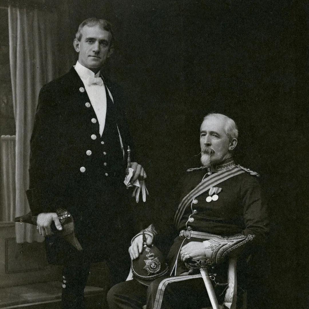A black and white photograph of two gentlemen, one seated and one standing