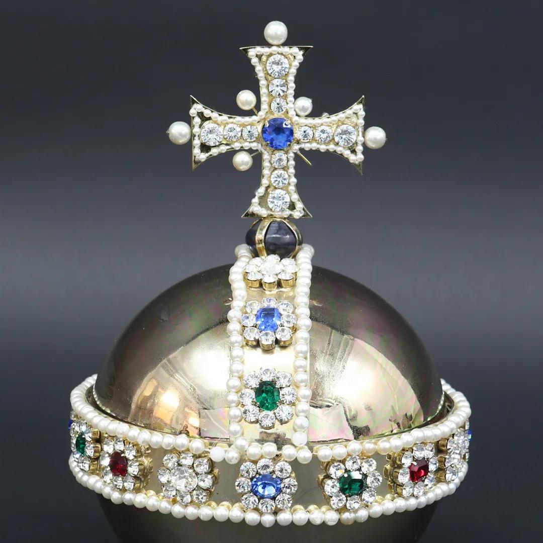 A colour photograph of a royal orb, coloured in gold with green and blue gems