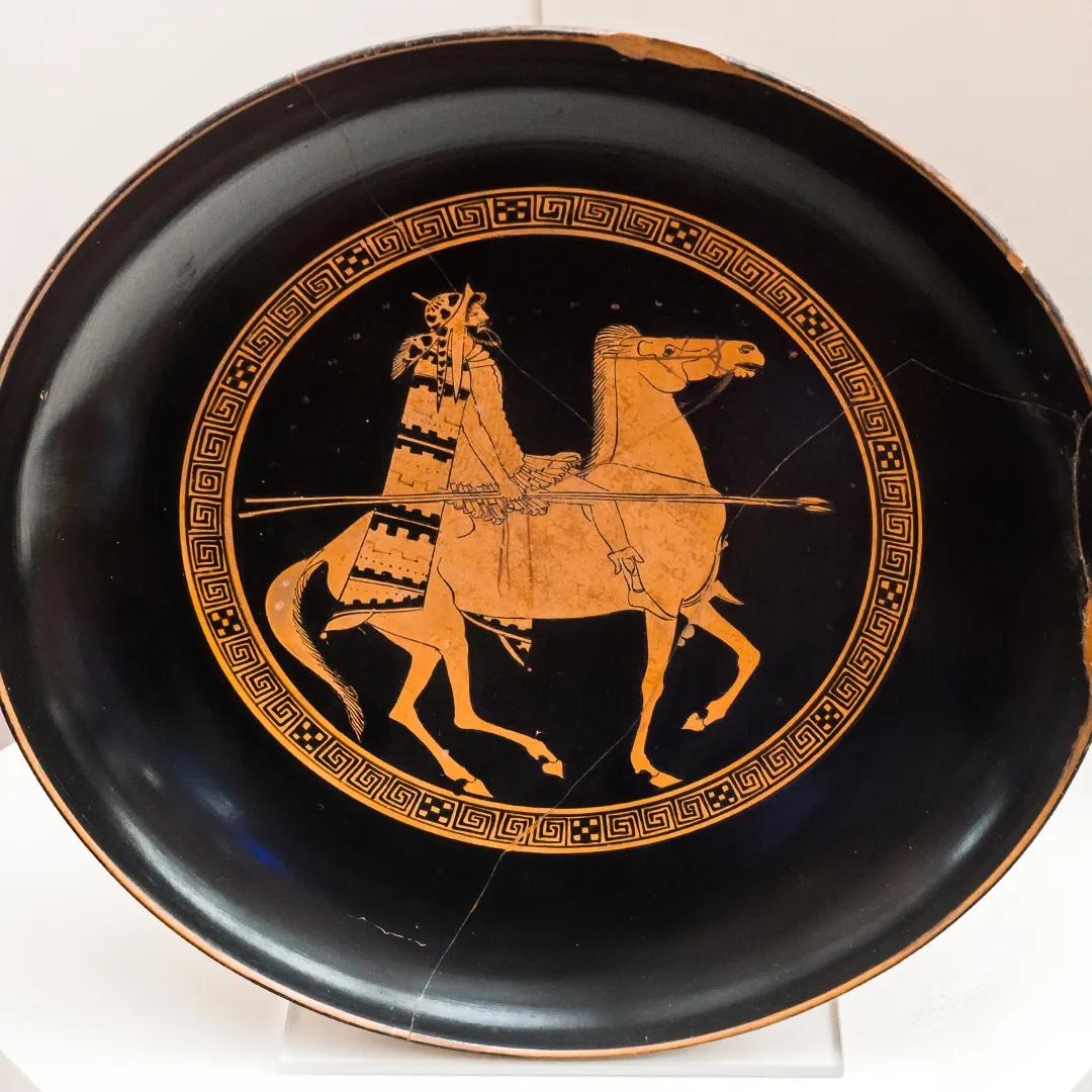 A black and red coloured dish with a glazed painting of a warrior on horseback