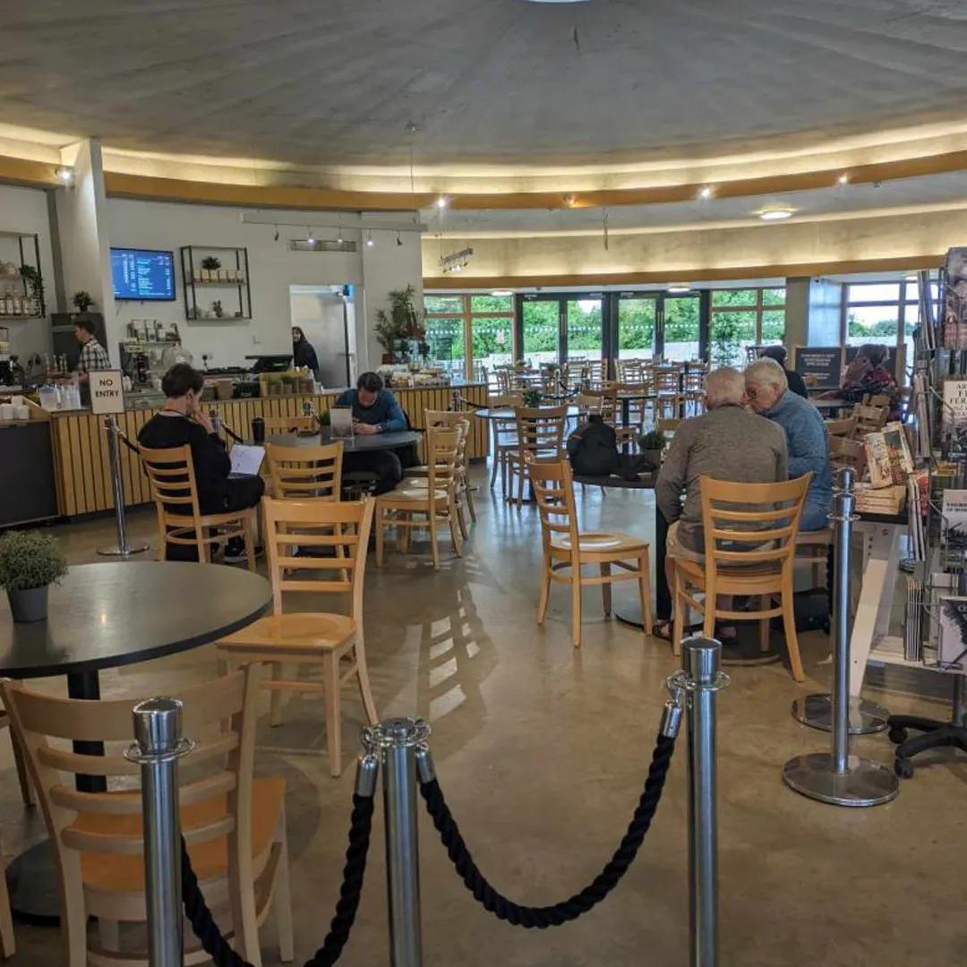 A photo of a cafe with wooden chairs and tables on a concrete floor