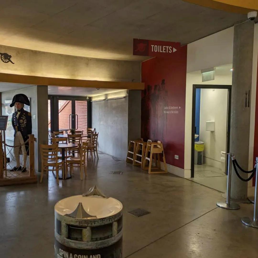 A photo of a concrete wall with a door and sign showing where the toilets are located
