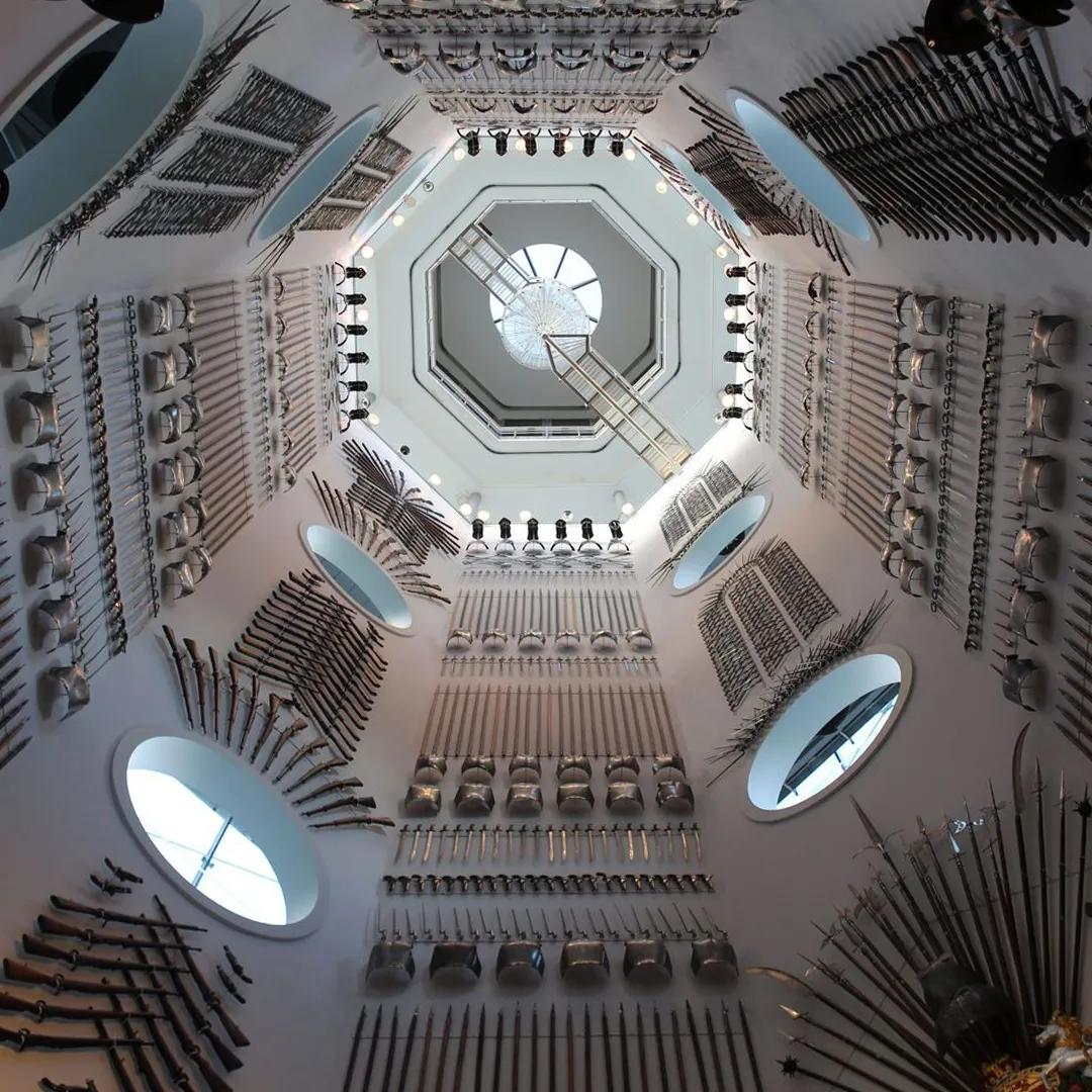 A large octagonal room with rows of armour and weapons lining the walls 