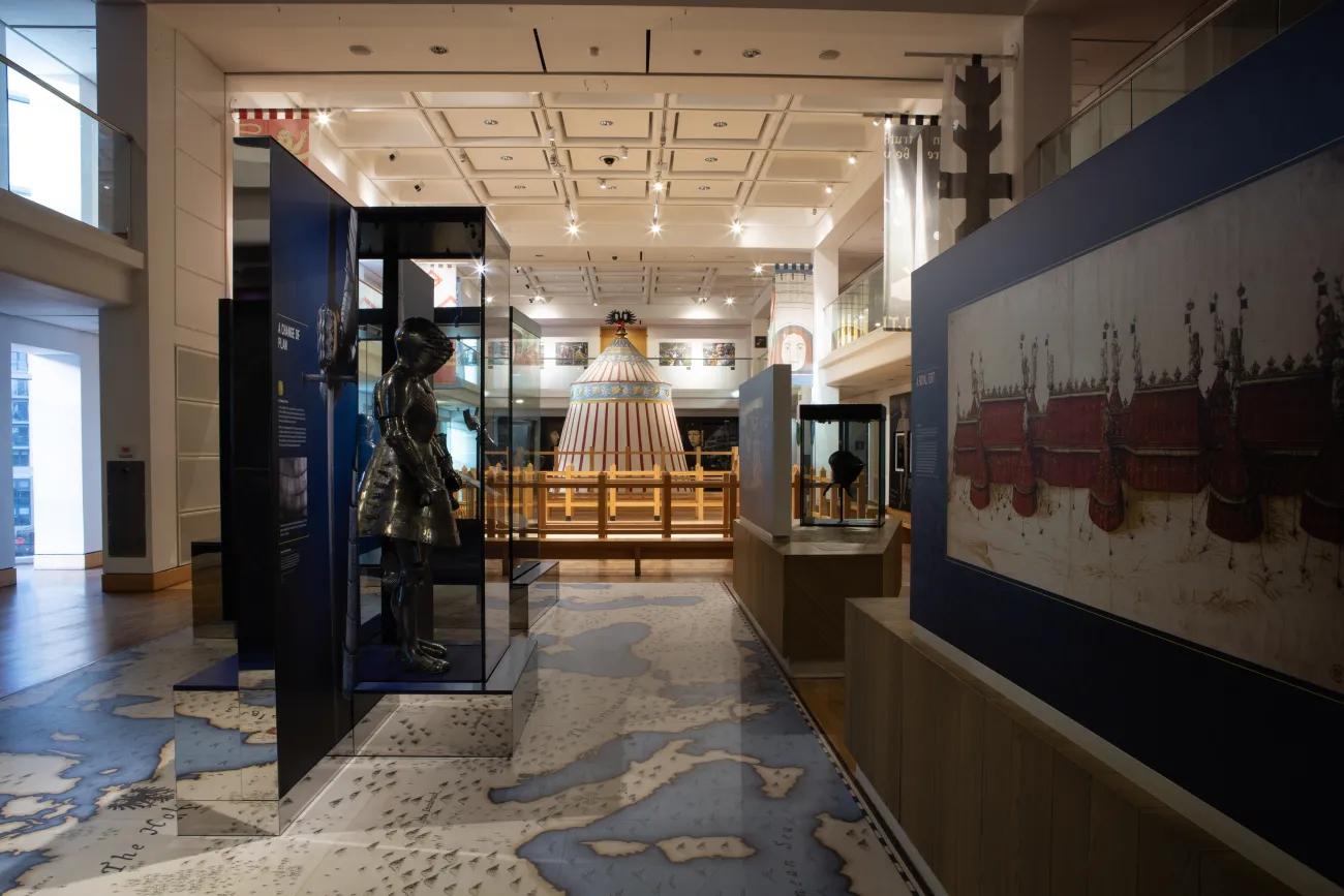 A photo of the tournament gallery on floor 2, featuring glass cases with full suits of armour and a duelling ring leading to a red and white pavilion at the far end of the room. 