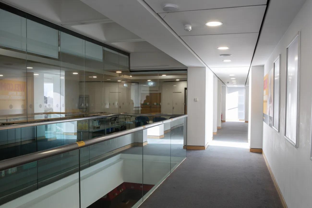 A long corridor leading away from the camera with an education room faced with glass on the left.