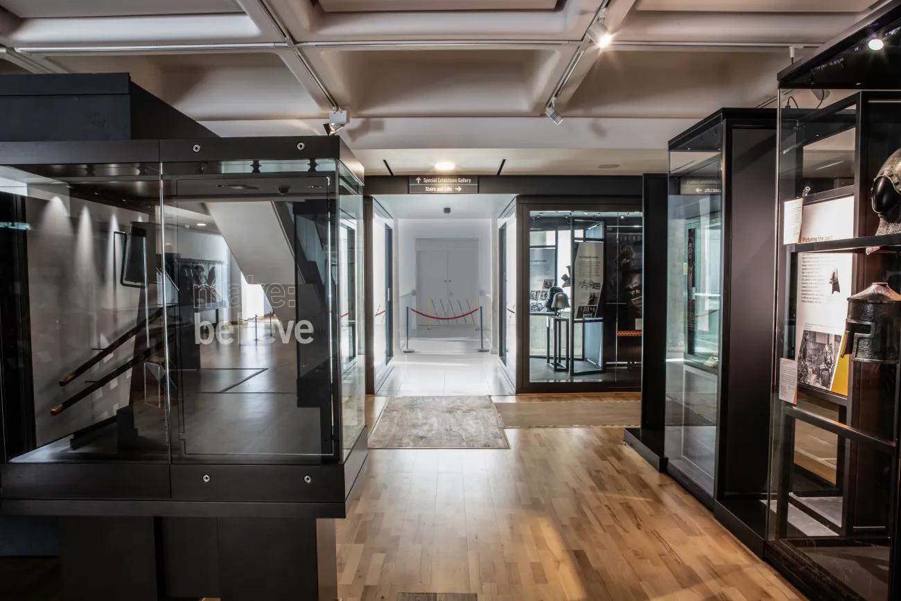 A darkened room with glass cabinets leads to an exit onto a bright corridor