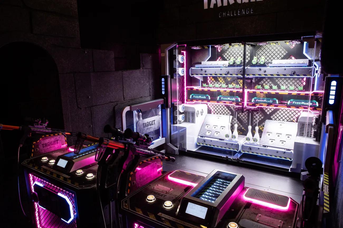 A neon coloured shooting range with fake assault rifles facing an assortment of targets.