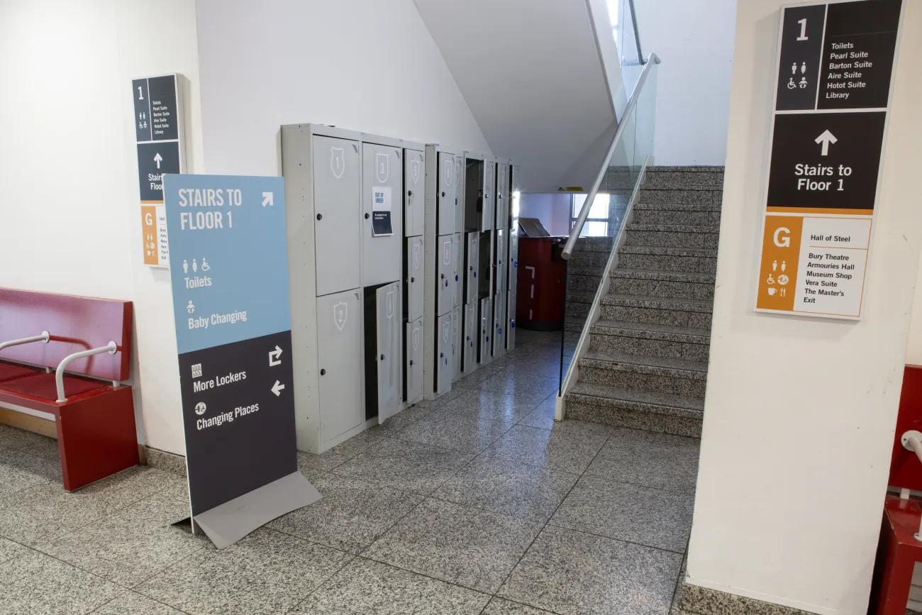 A flight of stairs disappear around a corner next to a bank of lockers