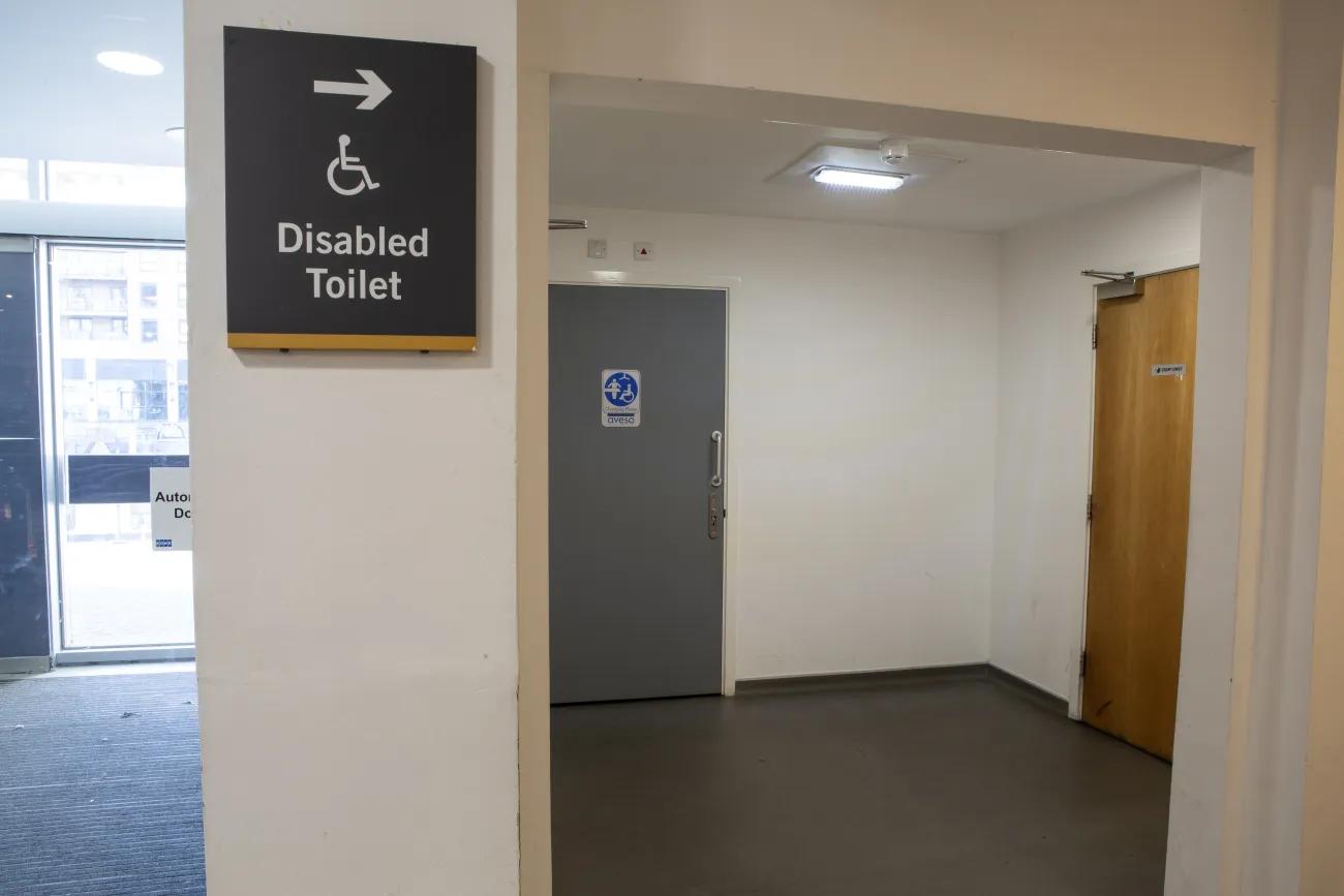 A disabled toilets sign indicating towards a grey door inside an alcove