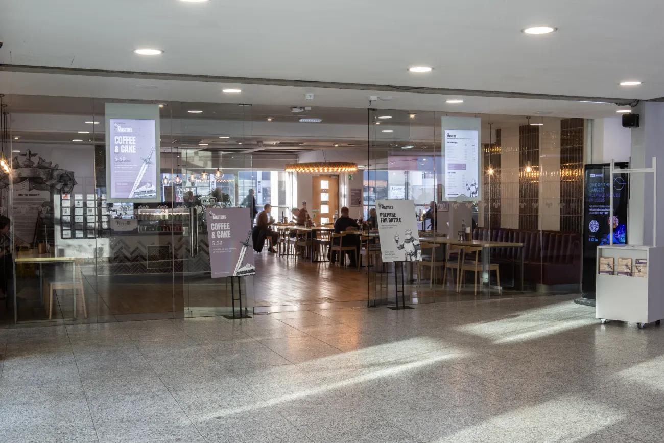 A glass fronted cafe with warm lighting inside and tables and chairs