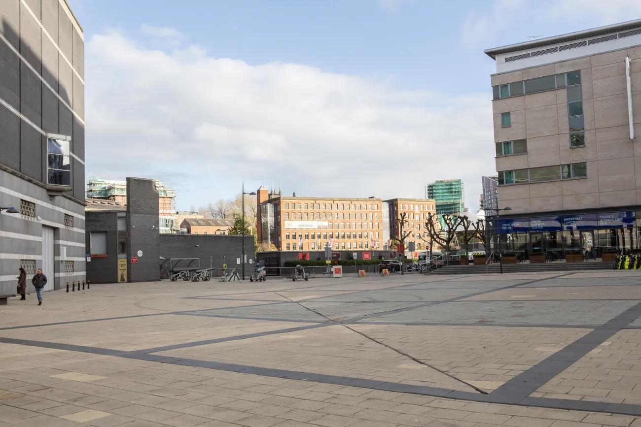 A wide open paved square leading to railings and a curve of cannons 