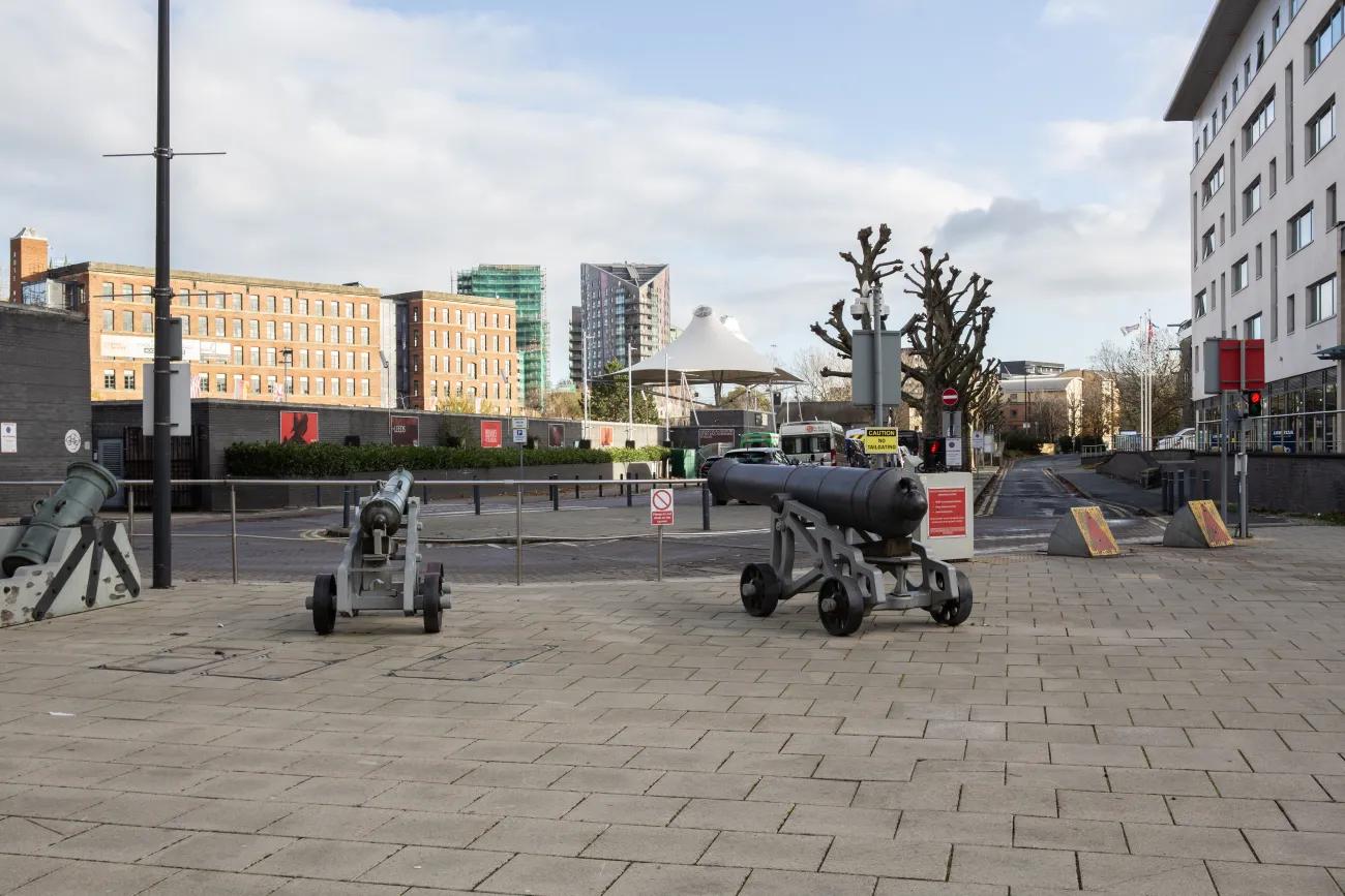 Cannons line a bend in the road leading towards a long dark grey wall