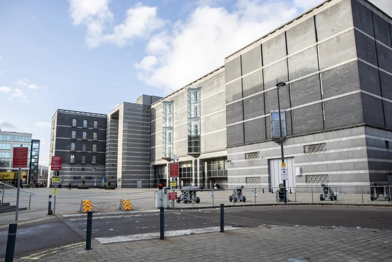 A colour photo of a large grey building with a row of cannons besides a line of bollards allowing access to a road