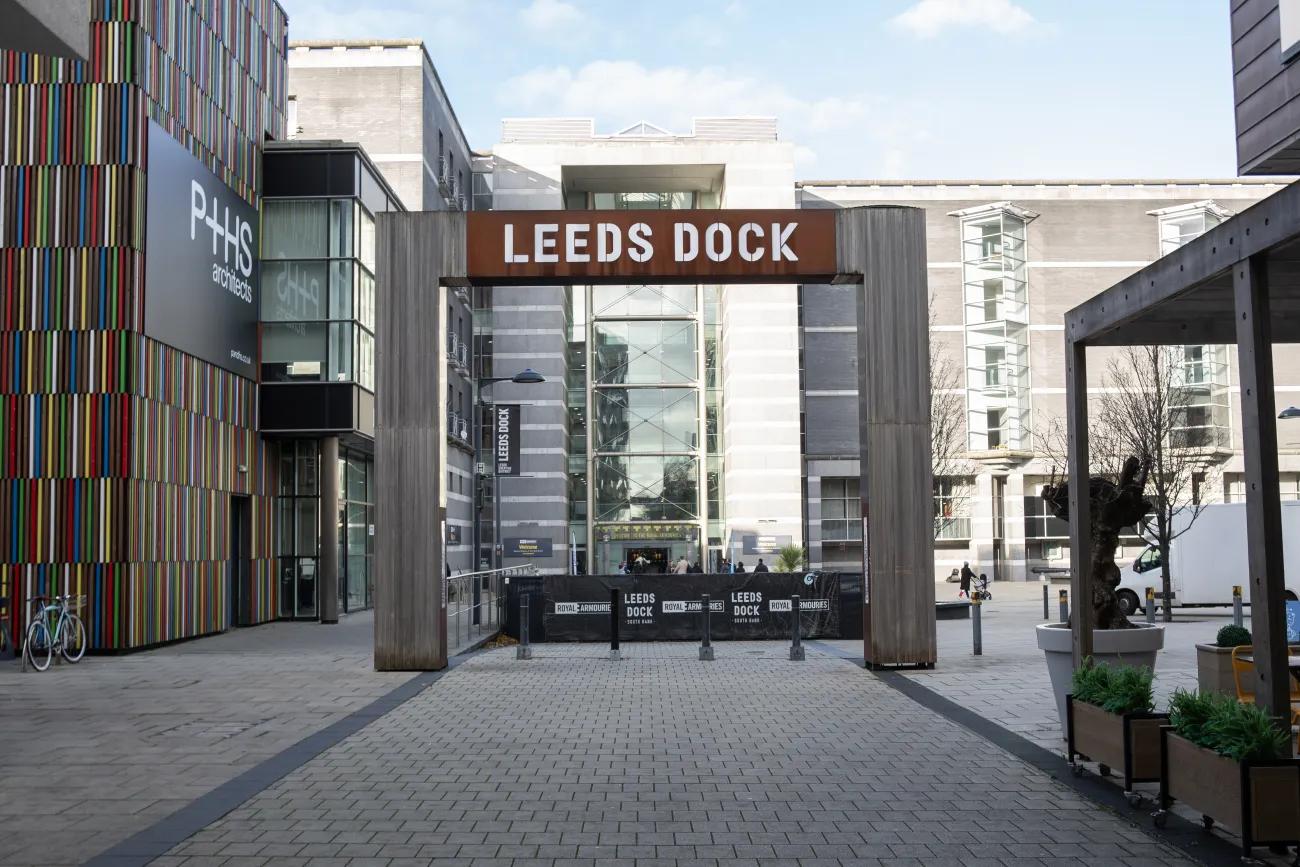 A colour photo of a wood and steel archway framing the entrance to a museum. Above it says Leeds Dock in white lettering.