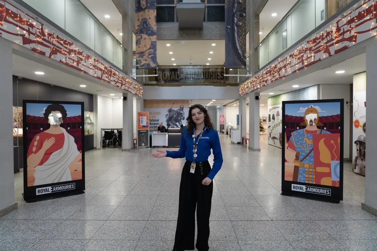 A woman in a blue uniform stands in a entrance hall greeting visitors