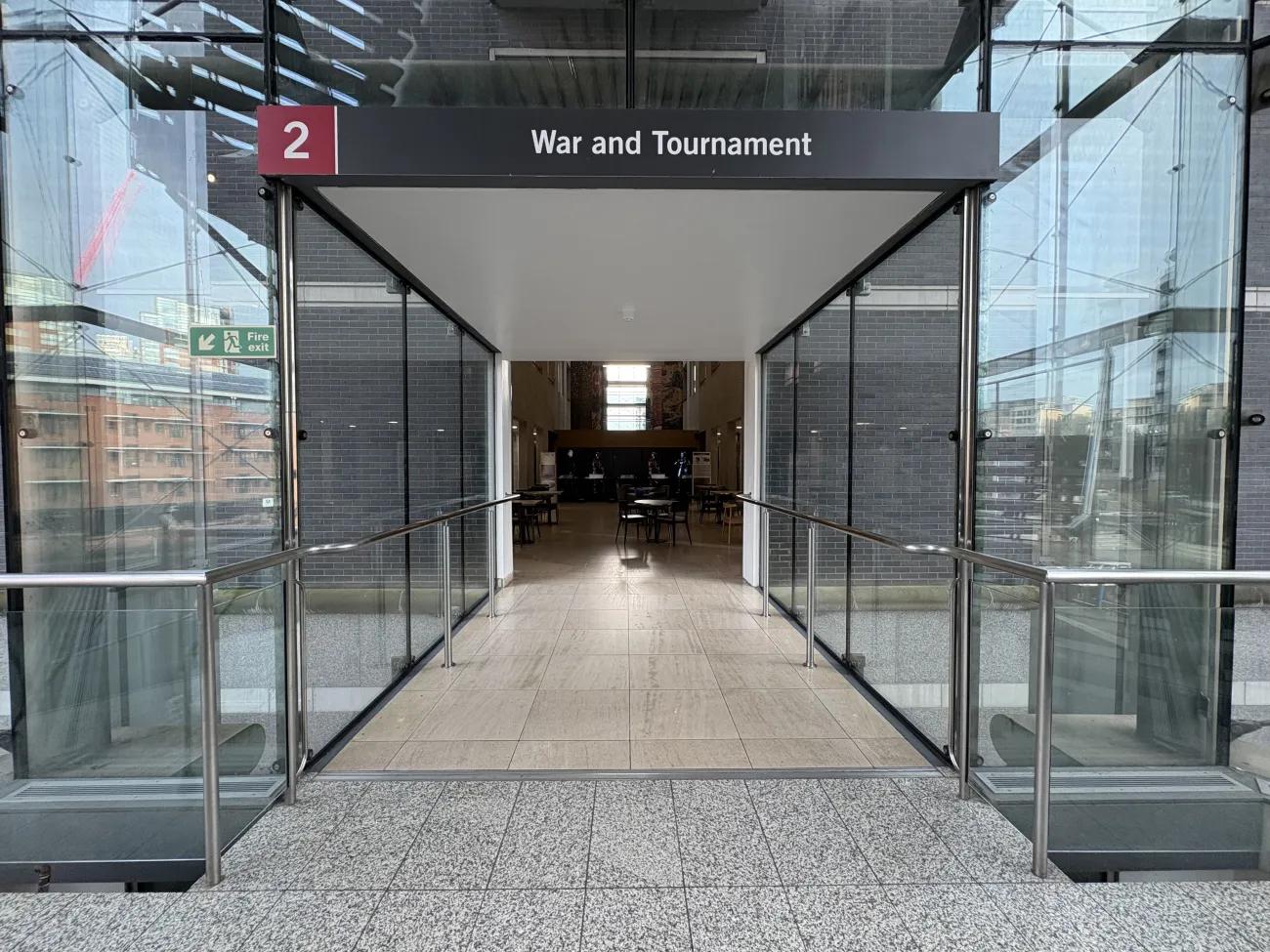 An entrance to a gallery floor about war and tournaments, framed in glass and steel