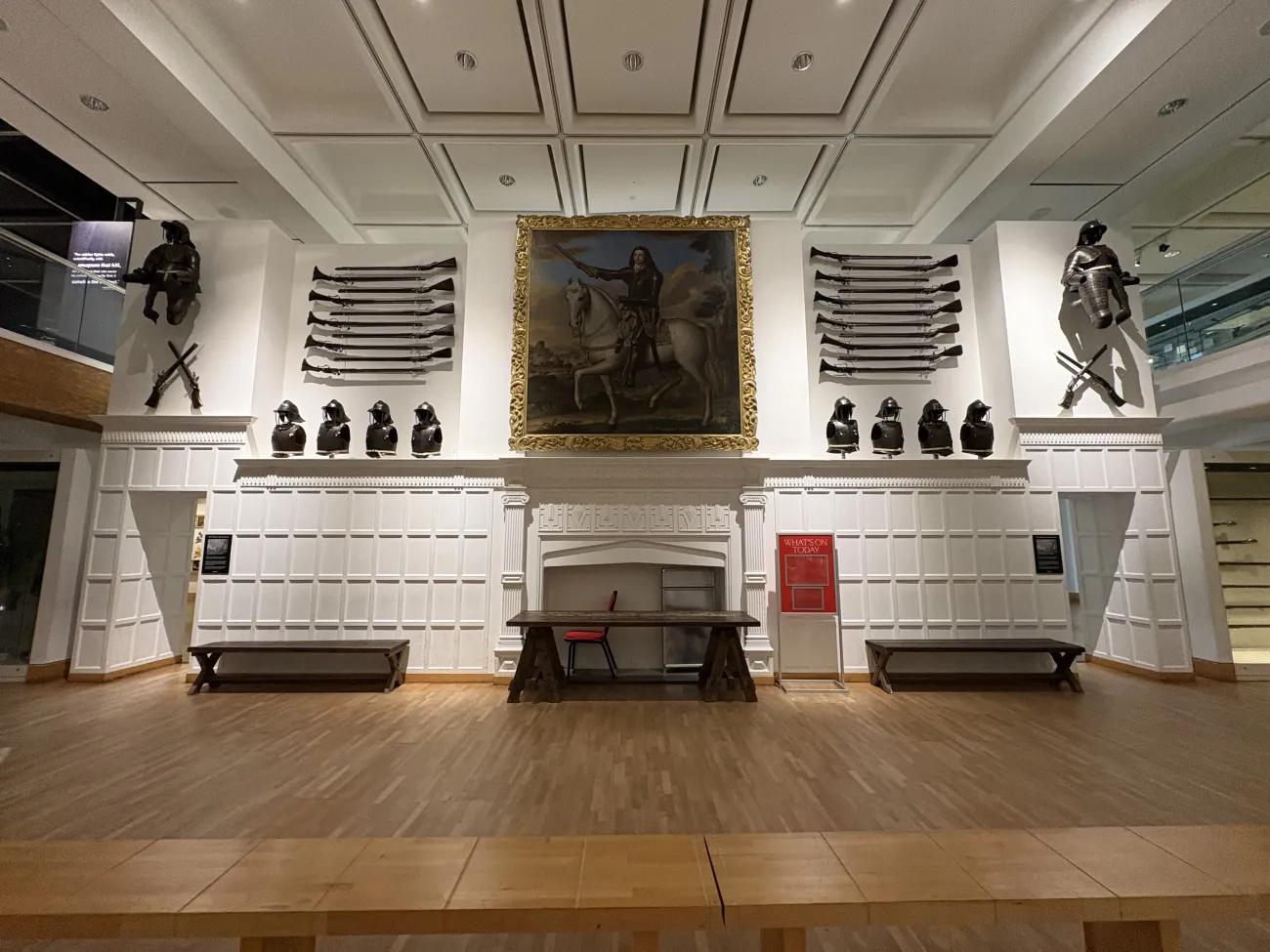 A wide-angle shot of the interior of the war gallery in the Royal Armouries, showing a white wall with arms and armour and a large painting of a 17th century officer on a horse